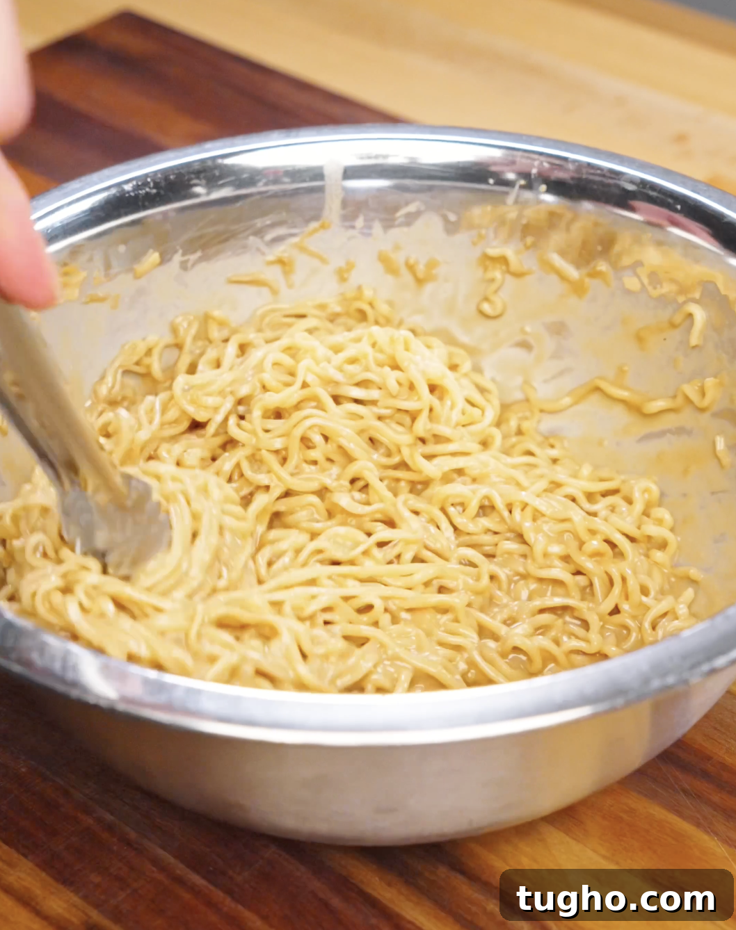 Creamy Sesame Noodles with Garlic Soy Sauce 7 Cooked noodles being tossed in a bowl with creamy sesame sauce until evenly coated.