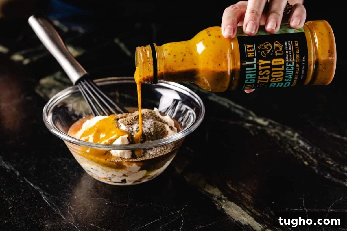 Tuna Macaroni Salad with Zesty Homemade Dressing Recipe 4 A bottle of Hey Grill Hey Zesty Gold BBQ Sauce pouring into a bowl of ingredients.