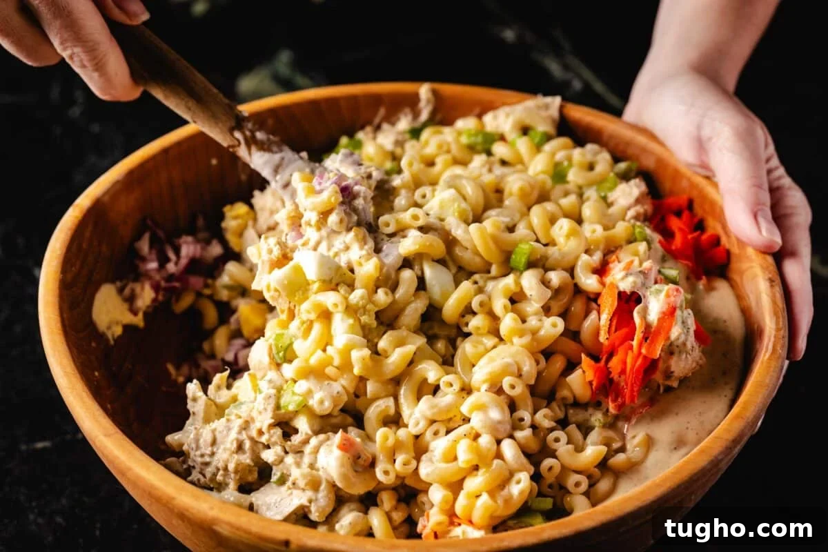 Tuna Macaroni Salad with Zesty Homemade Dressing Recipe 7 A hand using a wooden spoon to stir a macaroni salad in a wooden bowl.