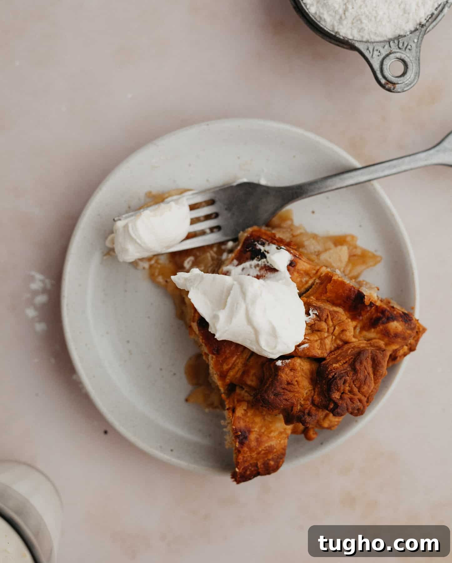 A slice of bourbon apple pie on a small plate. The pie has a dollop of whipped cream