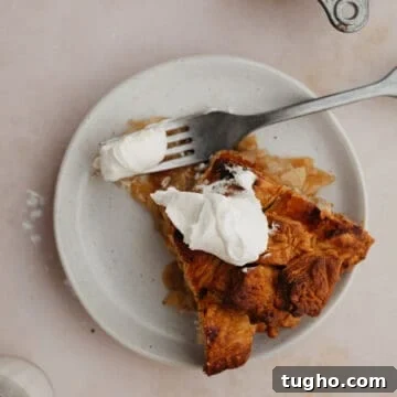 A slice of bourbon apple pie on a small plate. The pie has a dollop of whipped cream