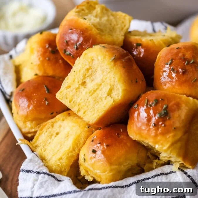 Pile of golden brown sweet potato dinner rolls topped with a garlic rosemary butter.