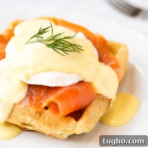 closeup of smoked salmon eggs benedict served on a dill waffle on a white plate.