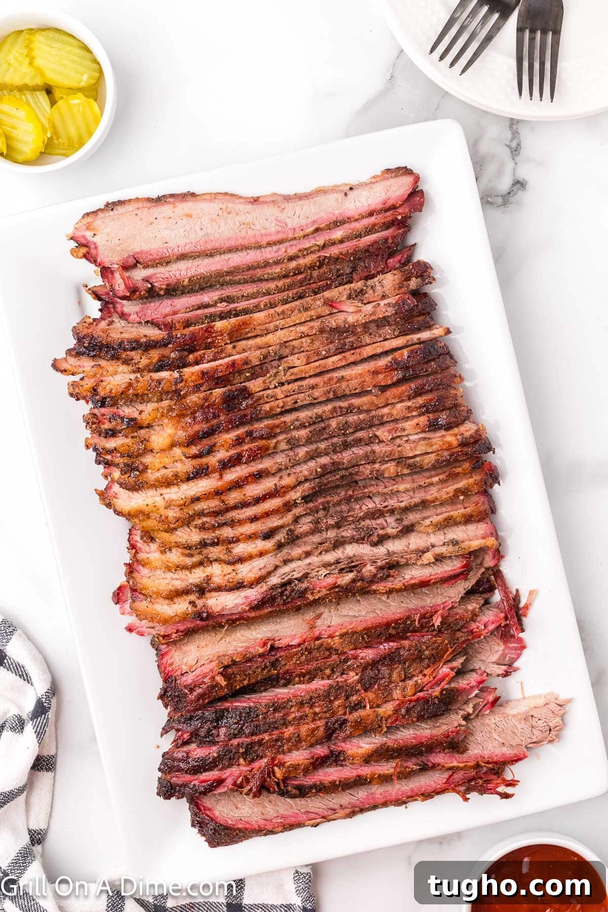 Authentic Texas Style Brisket Recipe 2 Sliced brisket on a white platter with a small bowl of sliced pickles on the side