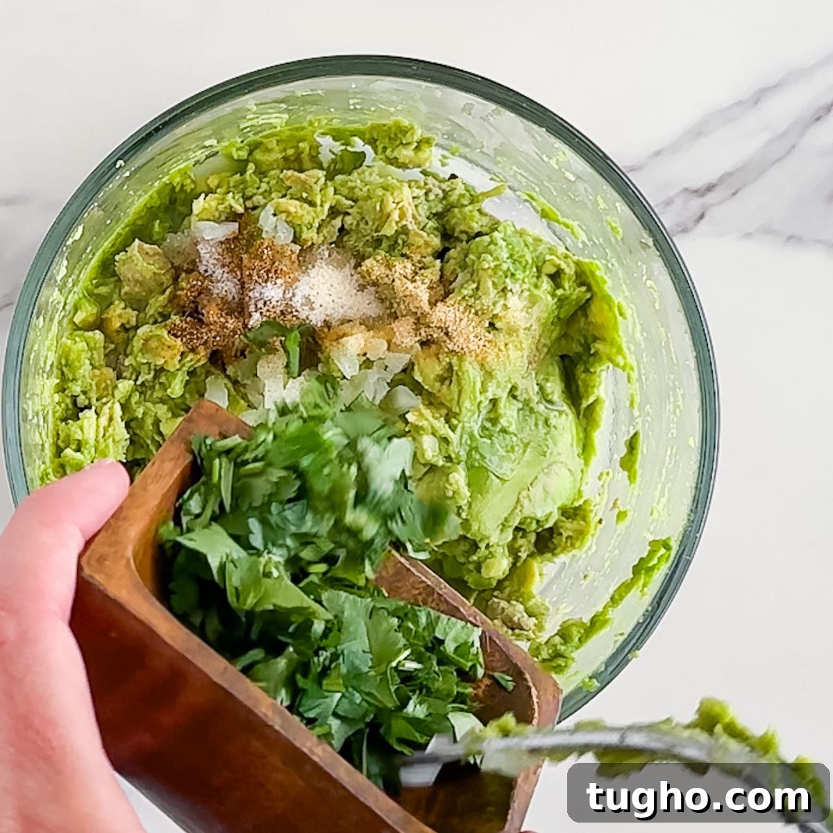 How to Make Authentic Mexican Guacamole with Lime and Cilantro 5 Adding the ingredients to smashed avocado.