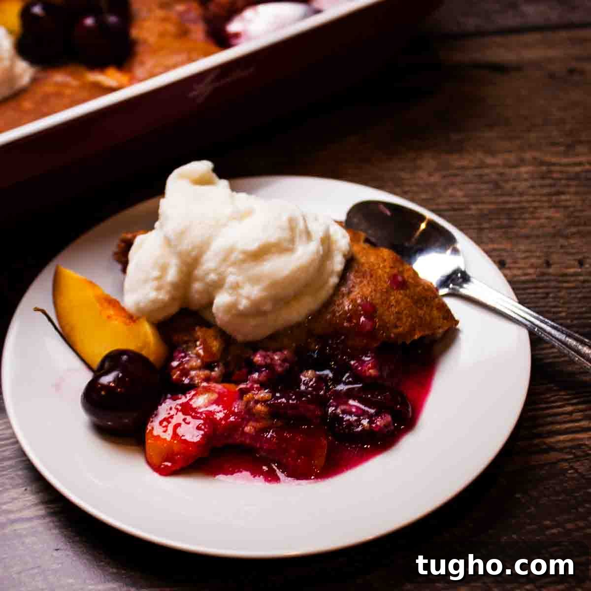 Homemade Cherry and Peach Cobbler Recipe 2 A serving of peach cherry cobbler on a dessert plate with a scoop of vanilla ice cream on top.