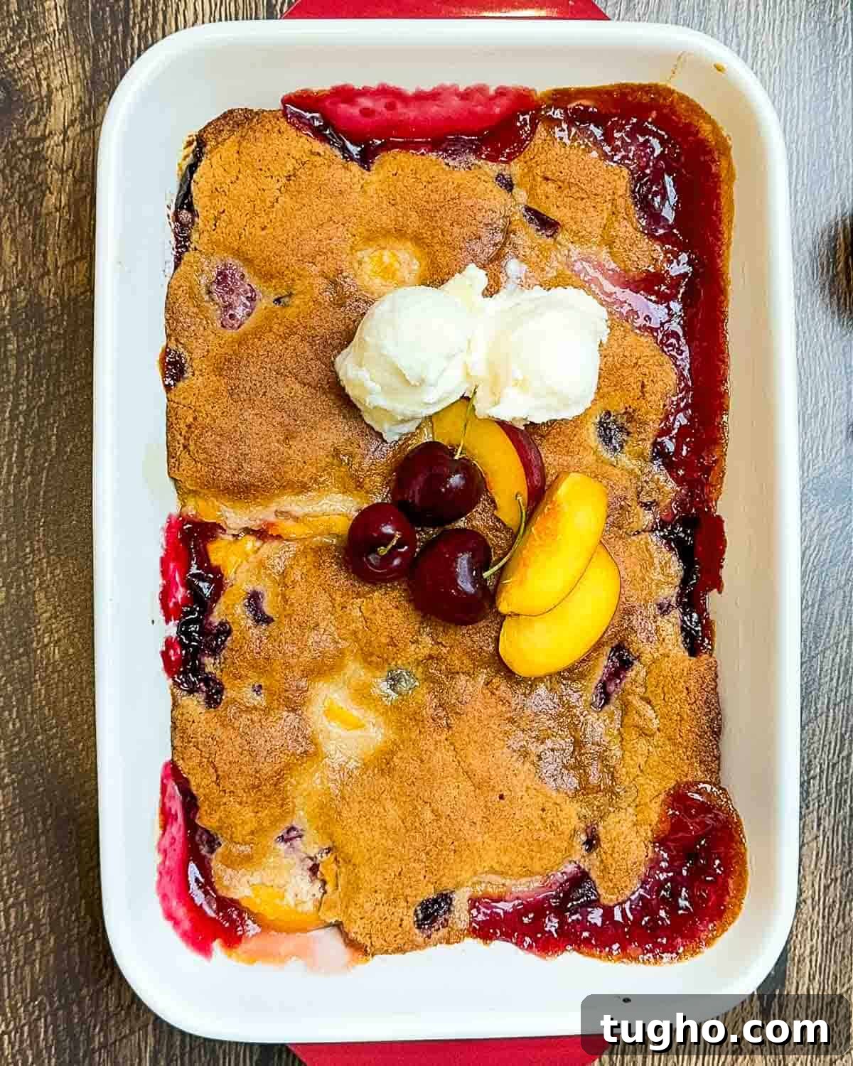 Homemade Cherry and Peach Cobbler Recipe 11 The baked cobbler in a baking dish garnished with vanilla ice cream, cherries, and peach slices.
