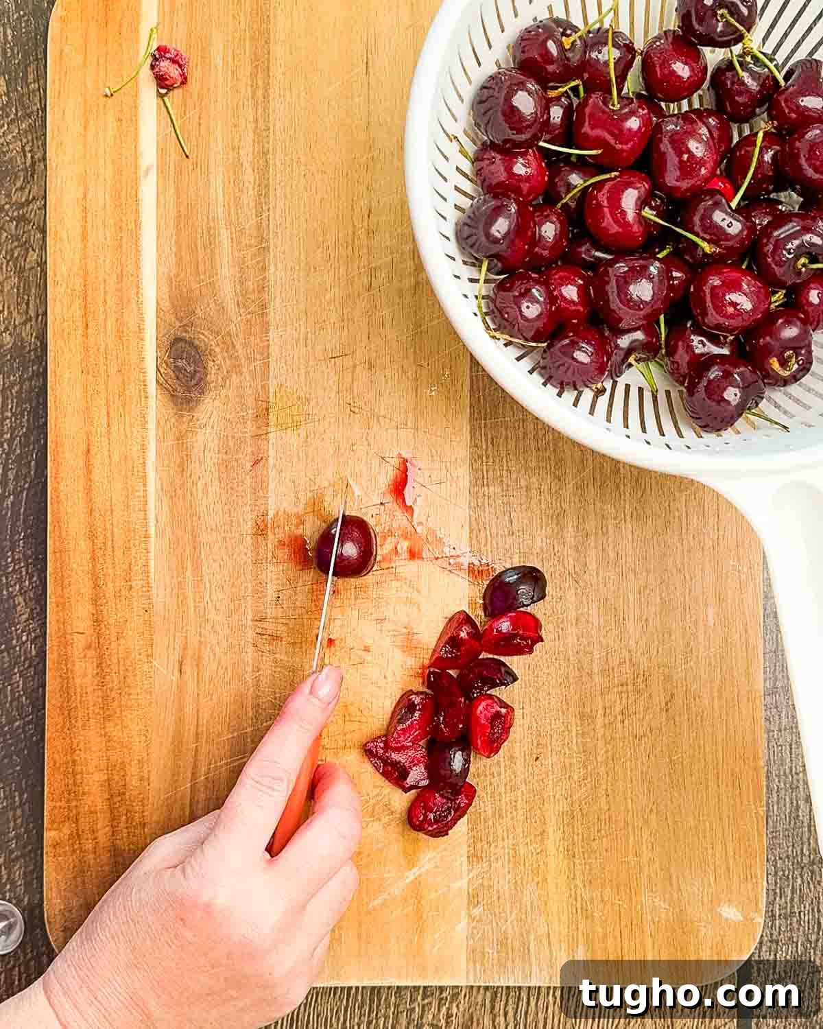 Homemade Cherry and Peach Cobbler Recipe 4 A paring knife cutting into a whole fresh cherry on a cutting board.