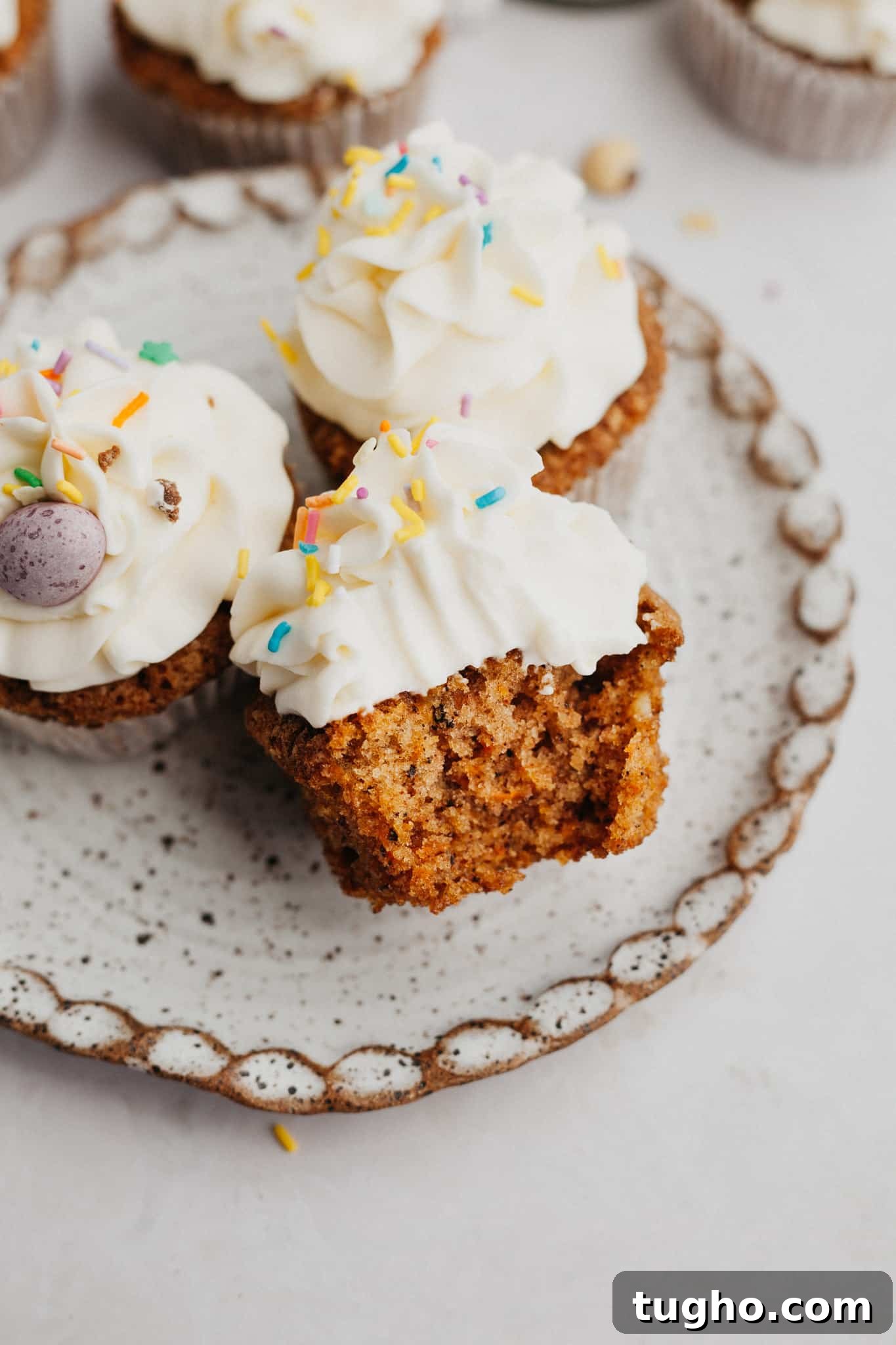 Moist Carrot Cupcakes with Cream Cheese Frosting 2 A small plate with three carrot cupcakes, one has a bite taken out of it.