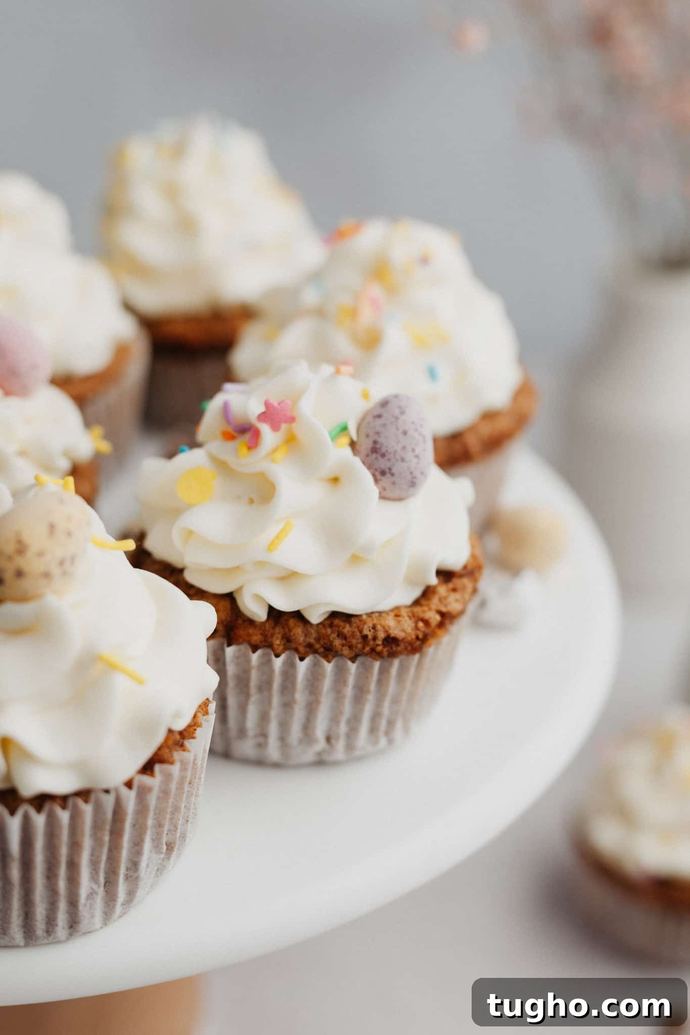 Moist Carrot Cupcakes with Cream Cheese Frosting 8 Several carrot cupcakes with white frosting on a cake stand.