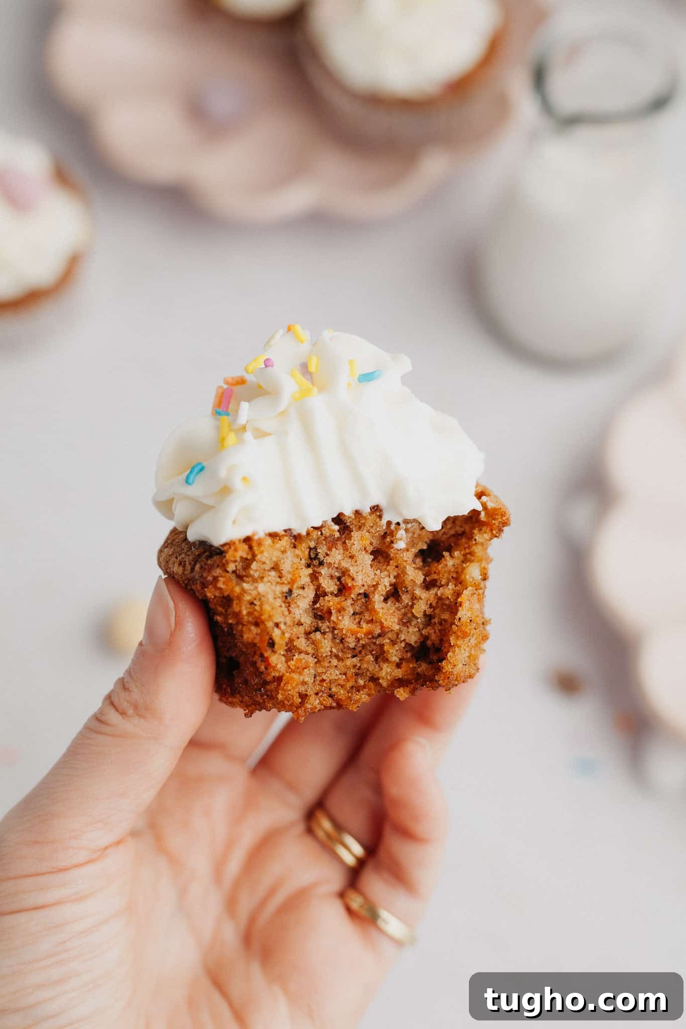 Moist Carrot Cupcakes with Cream Cheese Frosting 9 A hand holding a carrot cupcake with a bite taken out of it.