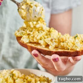 Woman spooning egg salad on bread.