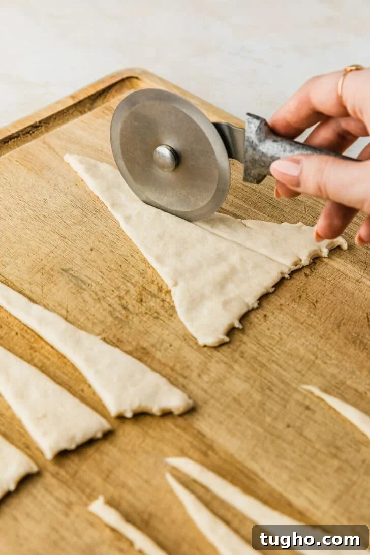 3-Ingredient Air Fryer Pigs in a Blanket Recipe 4 A hand using a pizza cutter to cut rolls on a wood board.