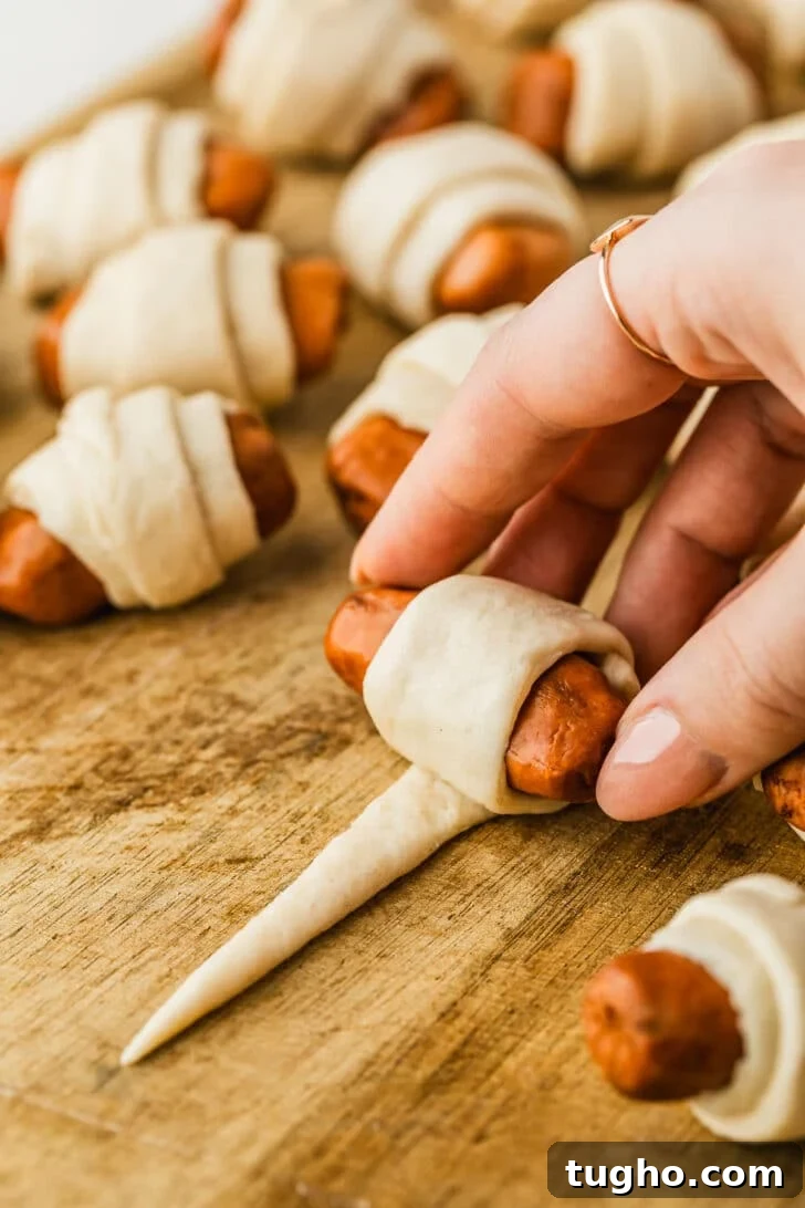 3-Ingredient Air Fryer Pigs in a Blanket Recipe 5 A hand rolling a mini sausage in dough on a wood board.