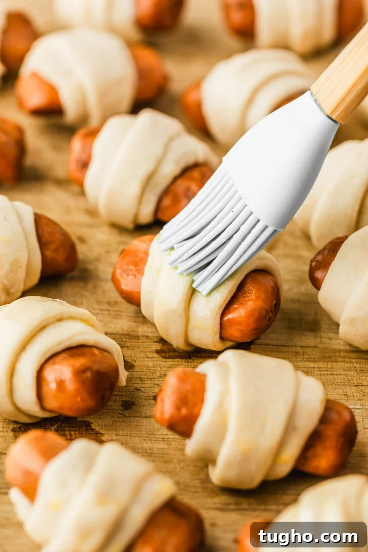 3-Ingredient Air Fryer Pigs in a Blanket Recipe 6 A pastry brush brushing egg wash on raw pigs in a blanket.
