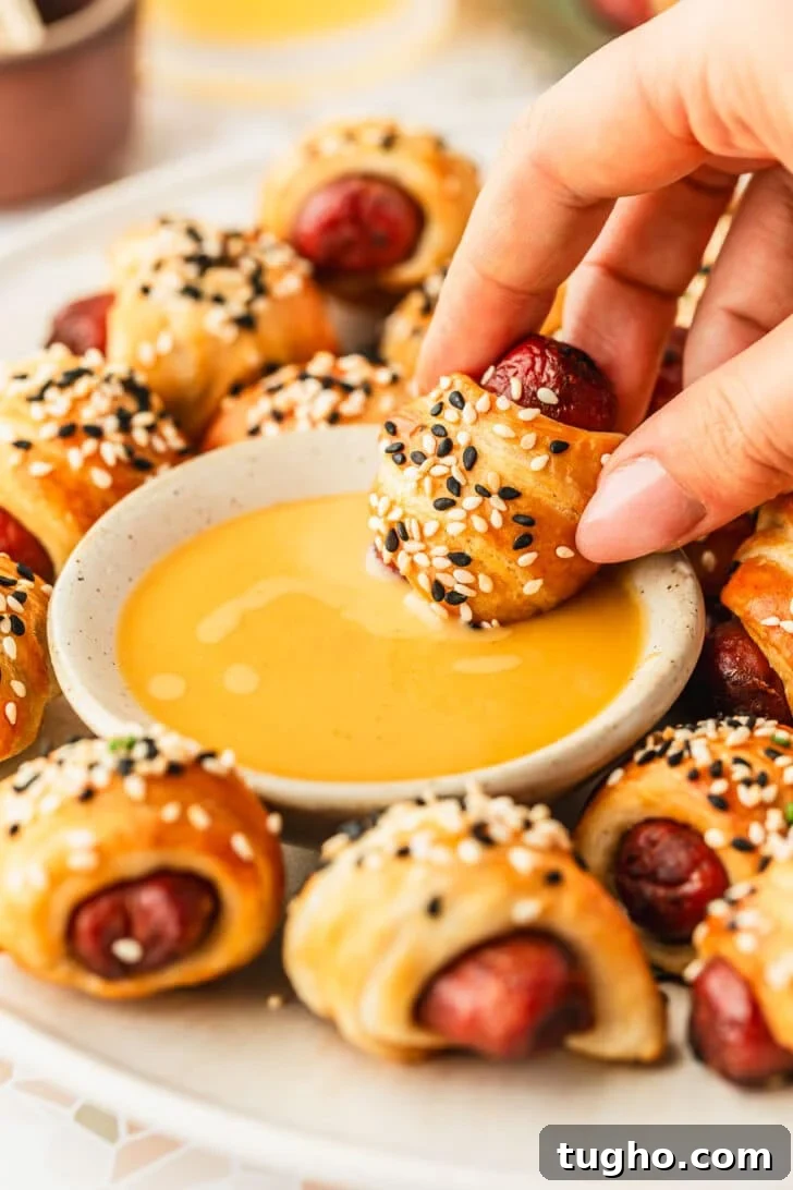 3-Ingredient Air Fryer Pigs in a Blanket Recipe 9 A hand dipping a pig in a blanket in mustard on a white platter of air fryer pigs in a blanket.