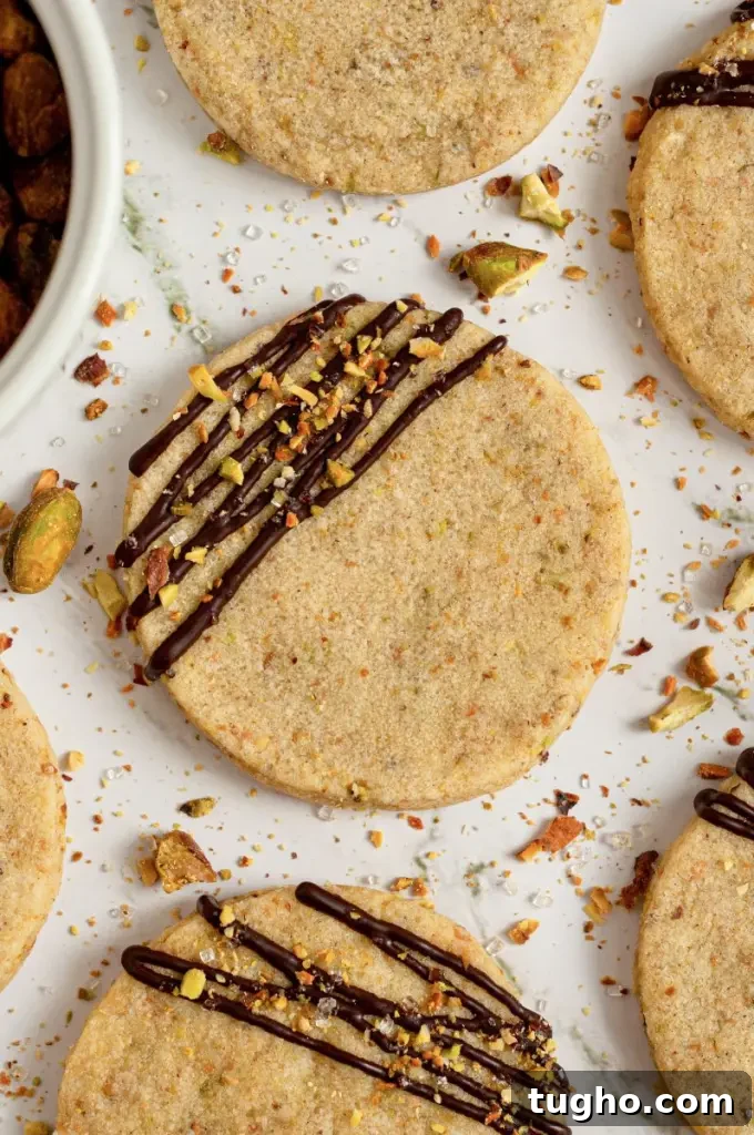 Light green pistachio shortbread cookies with a dark chocolate drizzle with sparkly white sprinkles and crushed pistachios on top of the chocolate.