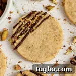Light green pistachio shortbread cookies with a dark chocolate drizzle with sparkly white sprinkles and crushed pistachios on top of the chocolate.