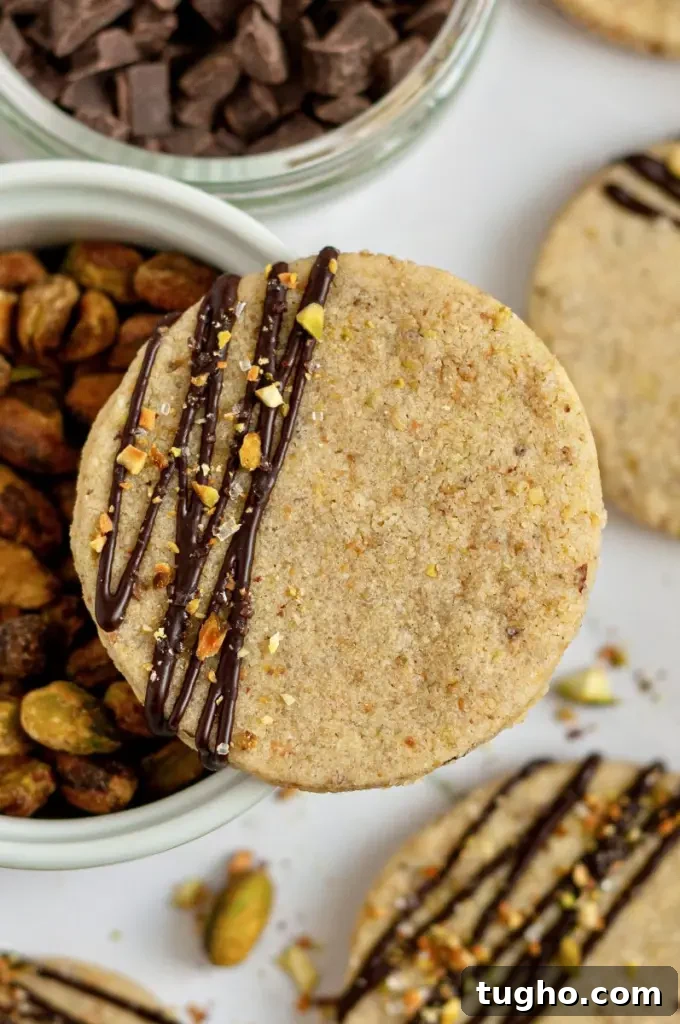 Light green pistachio shortbread cookies with a dark chocolate drizzle with sparkly white sprinkles and crushed pistachios on top of the chocolate.