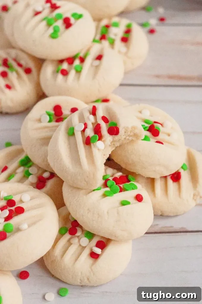 Perfectly round light yellow whipped shortbread cookies topped with red, white, and green confetti style sprinkles.