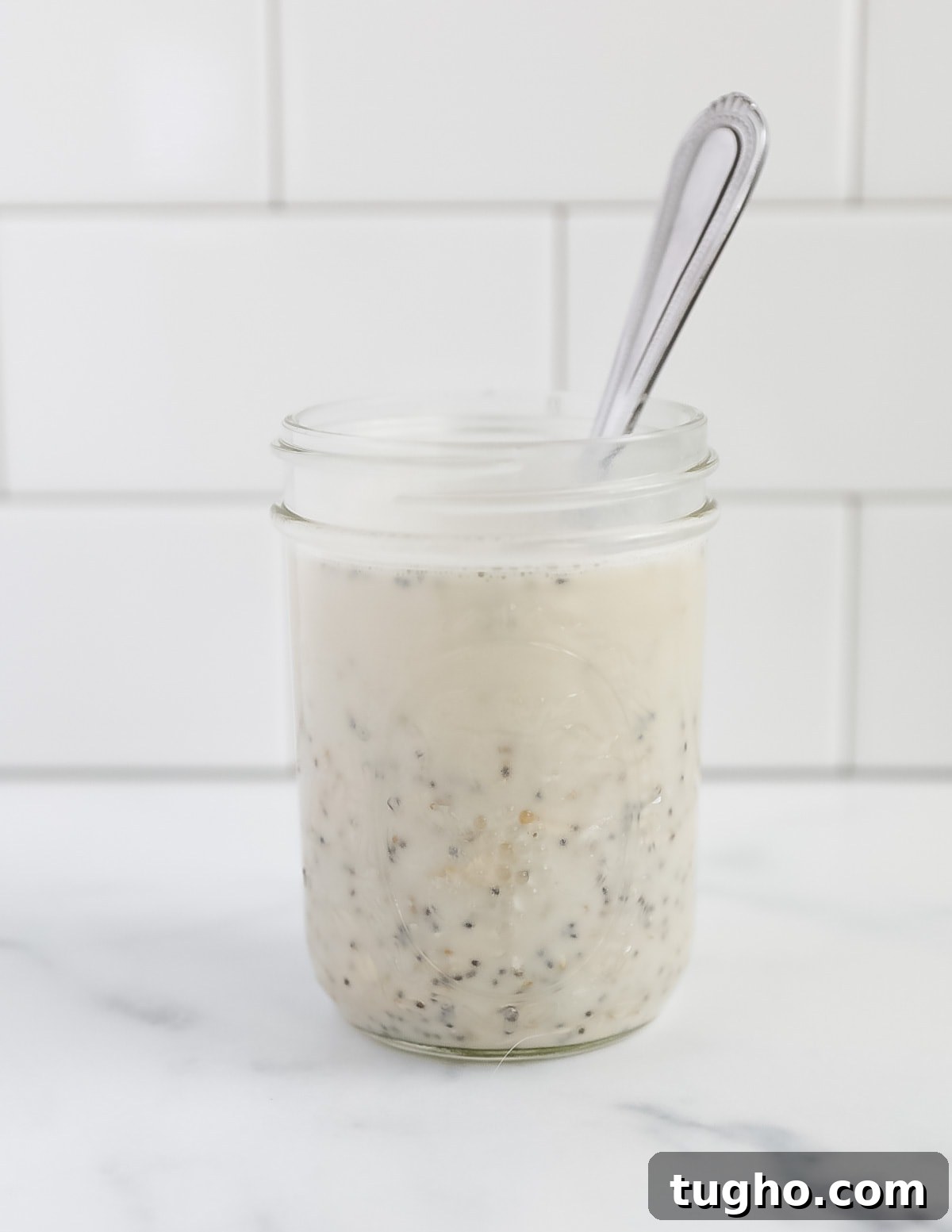 A mason jar with unmixed oats and plant-based milk, with a spoon inside