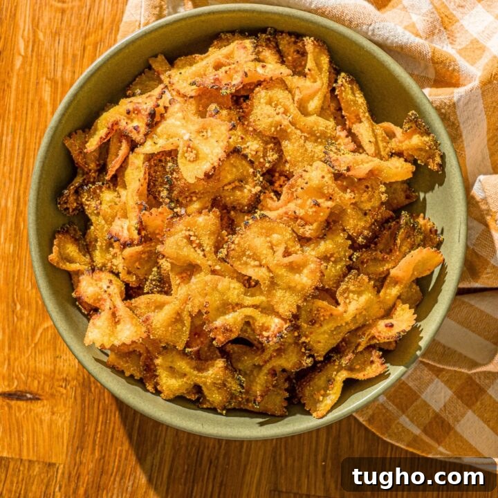 Crispy Baked Pasta Chips Recipe 12 Air fryer pasta chips that have mac and cheese seasoning on them in a green bowl on a wood counter.