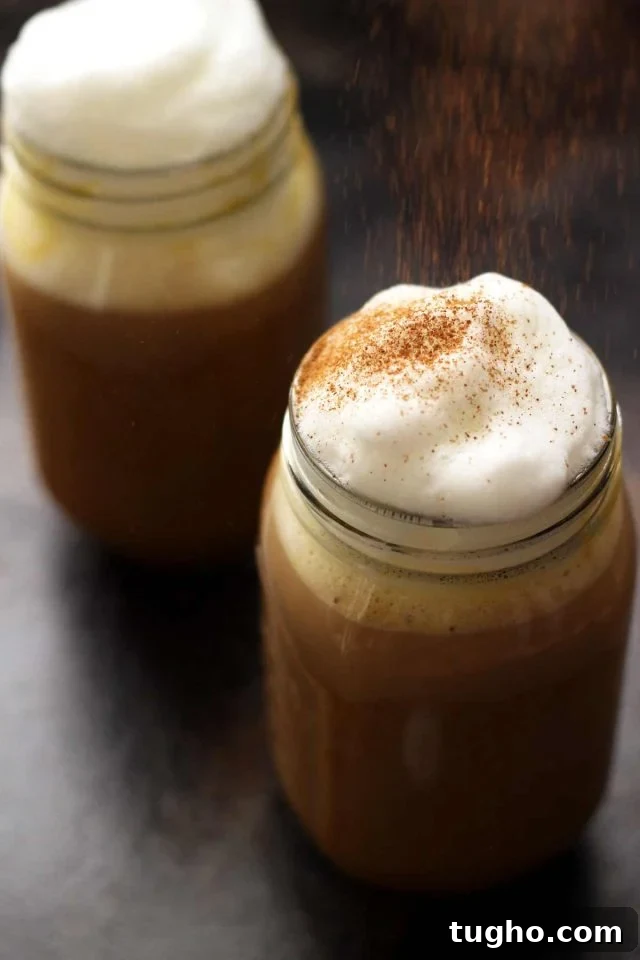 Creamy Vegan Pumpkin Spice Latte Recipe 2 Healthy Vegan Pumpkin Spice Latte in a Mason Jar Topped with Cashew Whipped Milk Being Sprinkled with Cinnamon