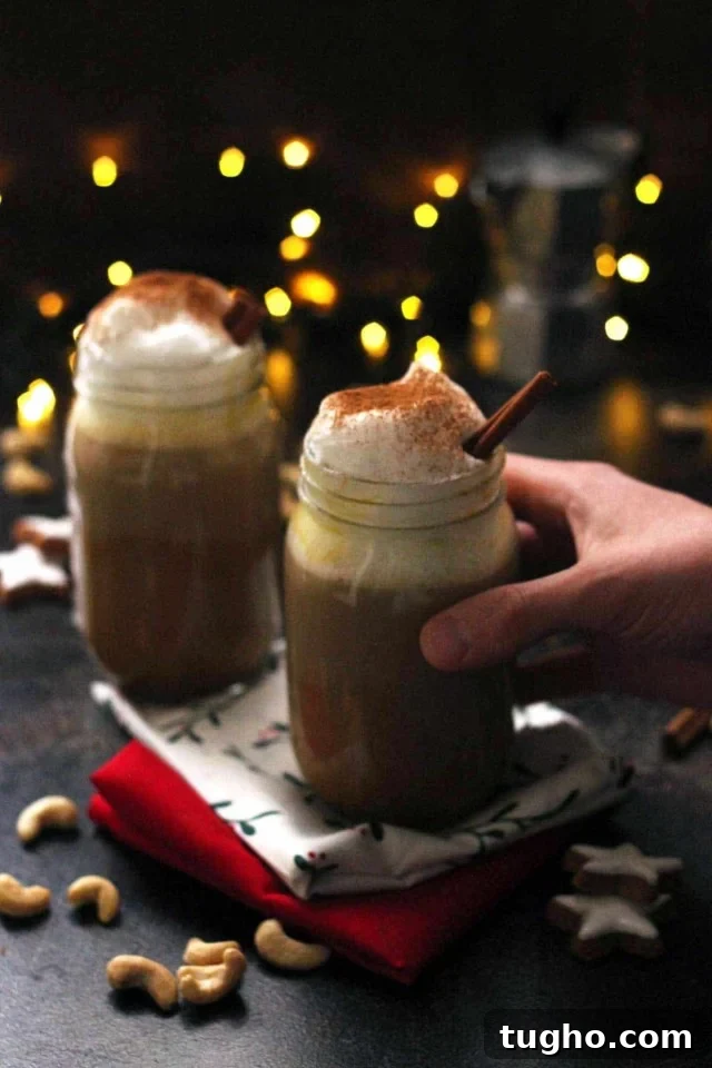 Creamy Vegan Pumpkin Spice Latte Recipe 6 Hand Holding a Glass of Healthy Vegan Pumpkin Spice Latte with Lights and Another Jar in the Background