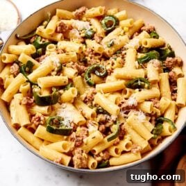 Marble surface with bowl filled with creamy sausage pasta with brown towel to the side.