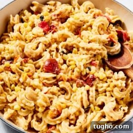 Large cooking pot filled with sweet corn pasta with pieces of cooked cherry tomato and wooden spoon resting against the side of the bowl.