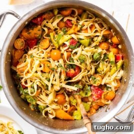 Large metal stockpot filled with pasta mixed with herbs and tomatoes all on marble surface.