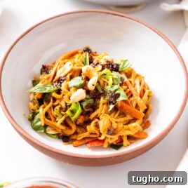 White bowl filled with spicy peanut noodles sitting on white countertop with basil and peanuts on top.