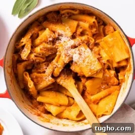 Top down view of large kettle sitting on white countertop filled with orange colored squash pasta with wooden spoon inside