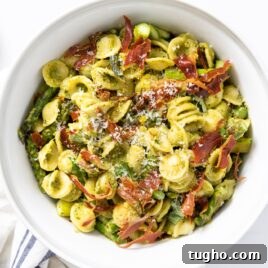 Top down view of yellow pasta covered in pesto sauce and topped with pieces of crispy prosciutto all on white countertop