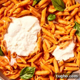 Roasted tomato pasta sitting in large brown bowl with balls of burrata cheese and fresh basil leaves.