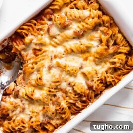 Top down view of white baking dish filled with pasta with red sauce and cheese all over the top with spoon sitting in dish