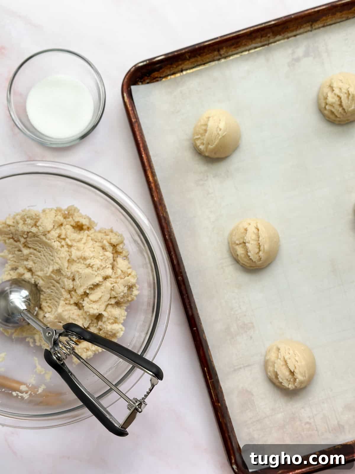 the cookie dough on a baking sheet with a bowl and cookie scoop to the side.