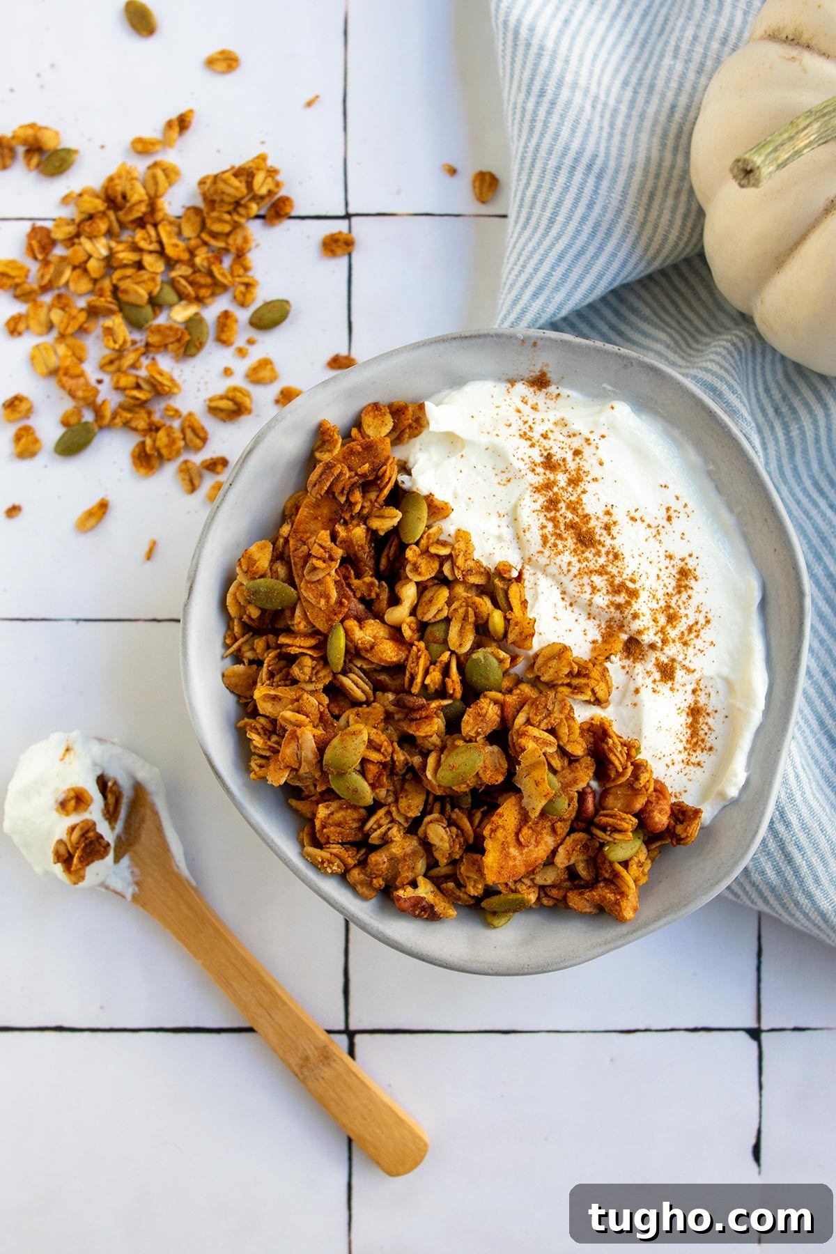 Pumpkin Granola Recipe with Maple or Date Syrup 9 A serving of granola in gray bowl with yogurt and cinnamon and a white pumpkin in the side.