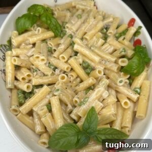 A white dish filled with creamy pasta mixed with green peas, garnished with fresh basil leaves.