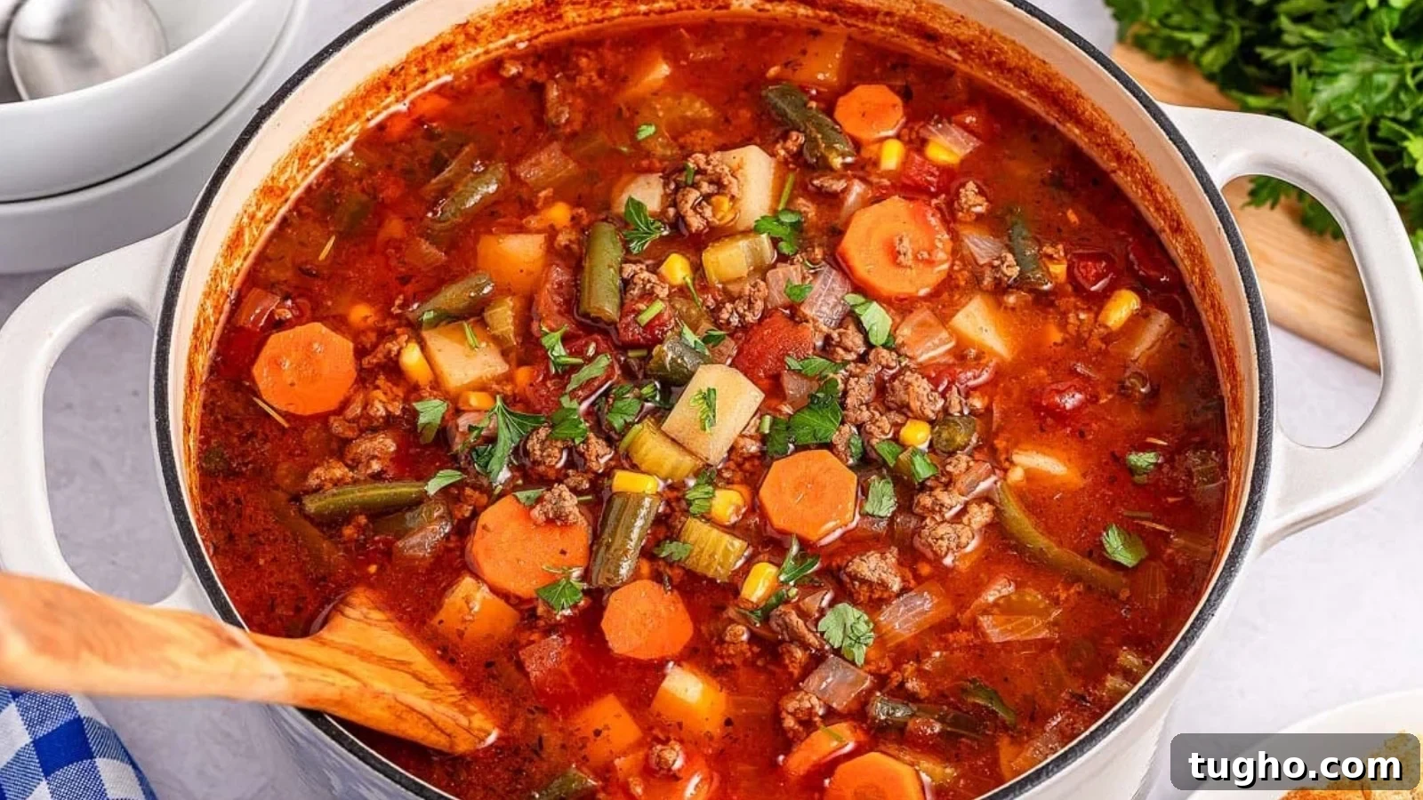 A pot of hamburger soup with carrots, corn, green beans, and meat in a tomato-based broth, garnished with herbs.