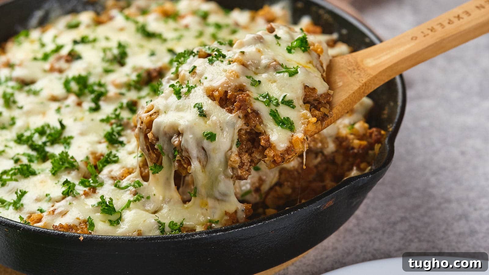 17 No-Fuss Dinners That Make the Whole Family Smile 4 A wooden spoon lifting a serving of italian ground beef skillet garnished with parsley from a cast-iron skillet.