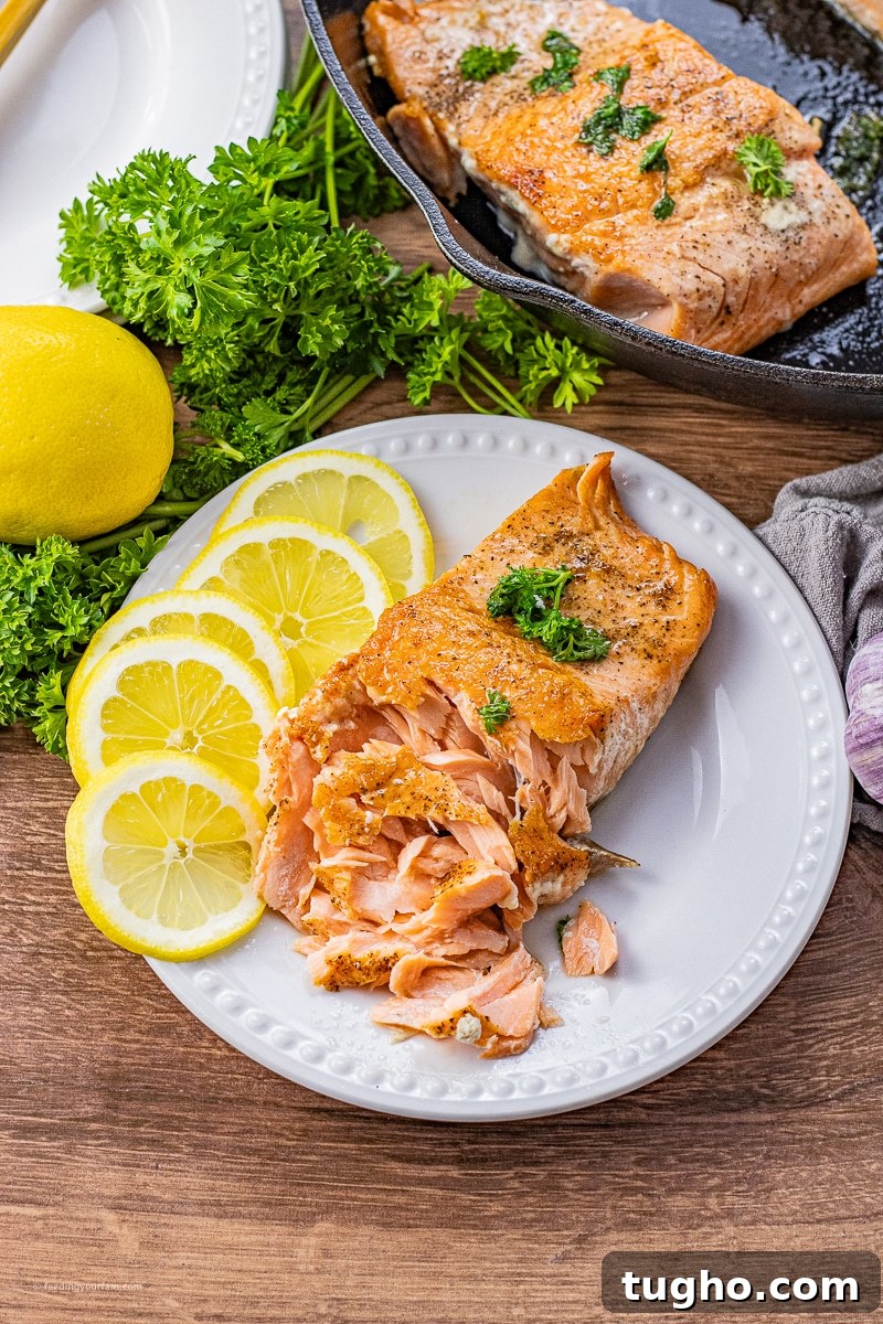 cast iron cooked salmon on a white plate with the salmon flaked a little bit with some lemon slices