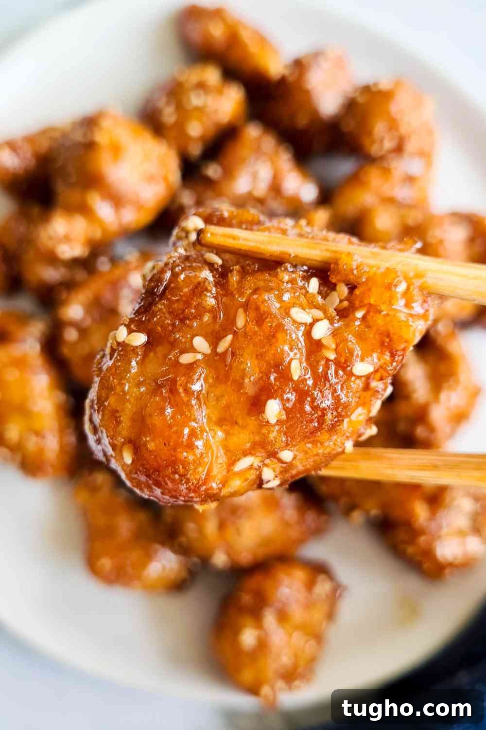Homemade Crispy Honey Sesame Chicken Recipe 13 A piece of crispy chicken bite being held up of a pair of chopsticks