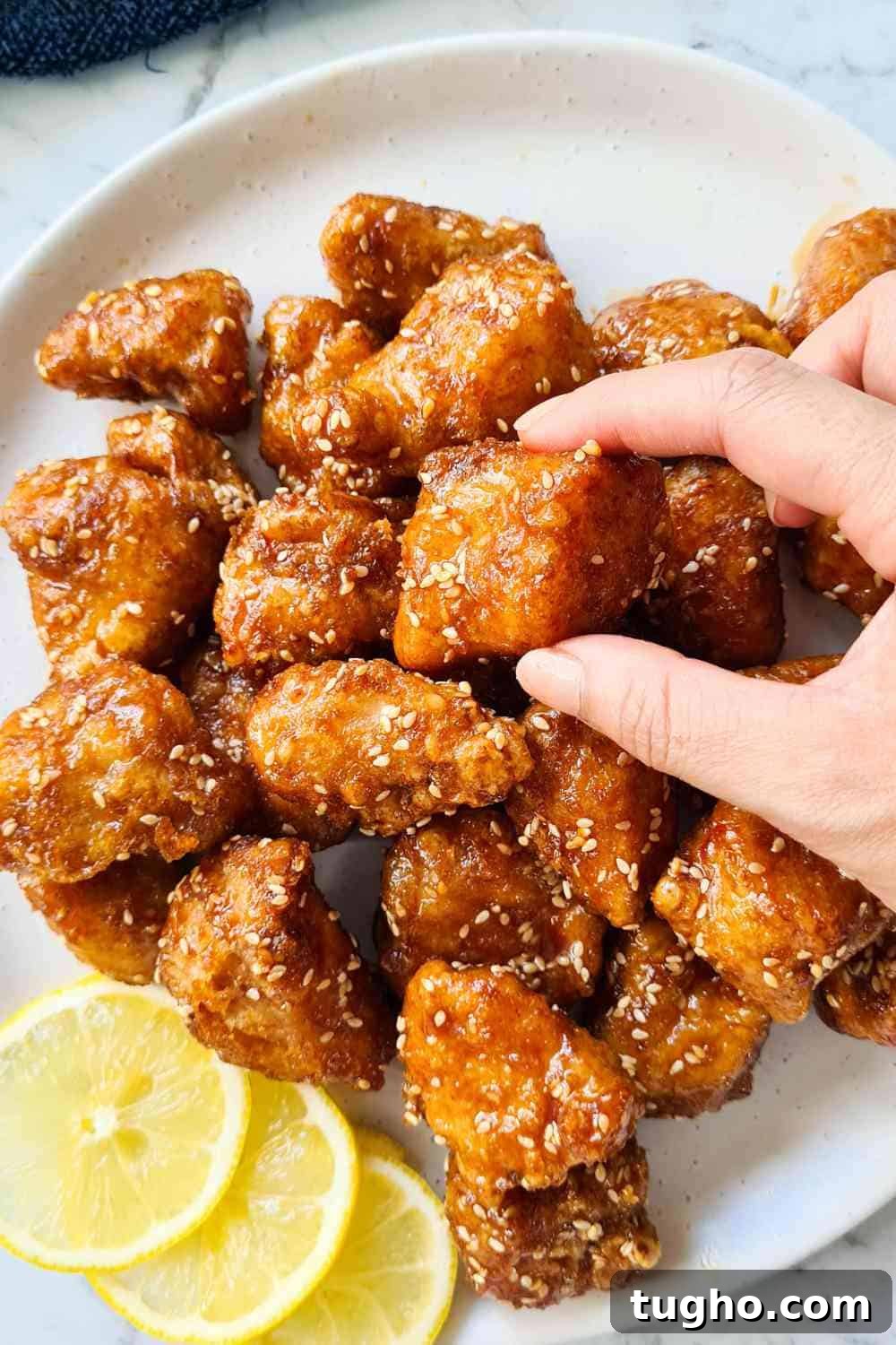 Homemade Crispy Honey Sesame Chicken Recipe 14 A piece of crispy chicken piece being picked up by two fingers