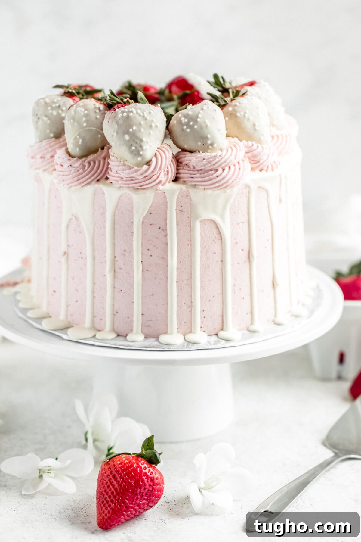 White Chocolate-Covered Strawberry Cake Recipe 3 strawberry and white chocolate cake on a cake stand with strawberries in the background