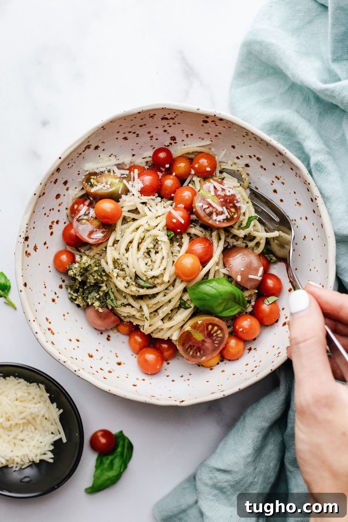 Pesto Spaghetti with Fresh Garden Tomatoes 2 Hand holding a fork in a ceramic bowl with spaghetti and cherry tomatoes.
