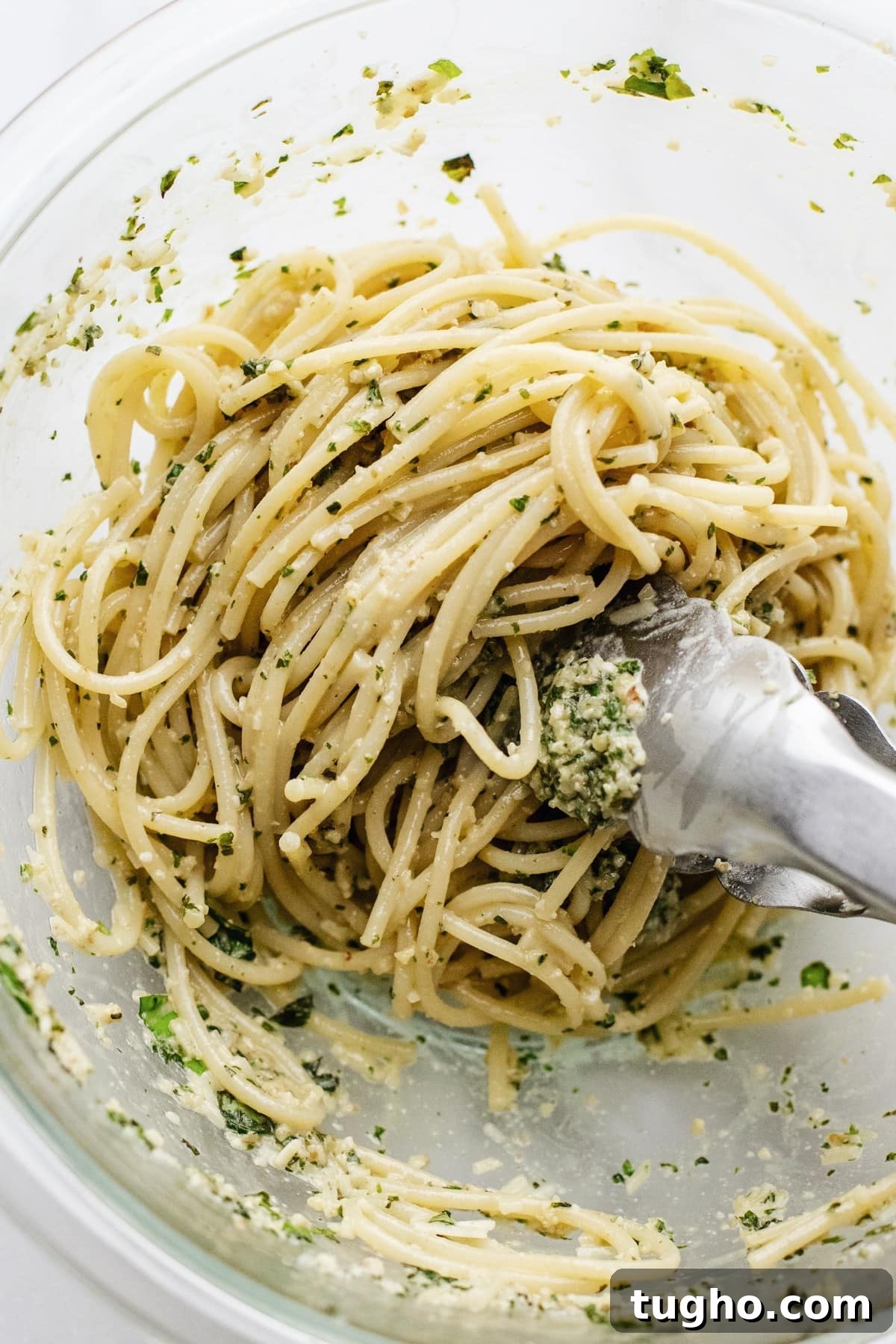 Pesto Spaghetti with Fresh Garden Tomatoes 5 Tongs tossing spaghetti in a clear glass bowl.