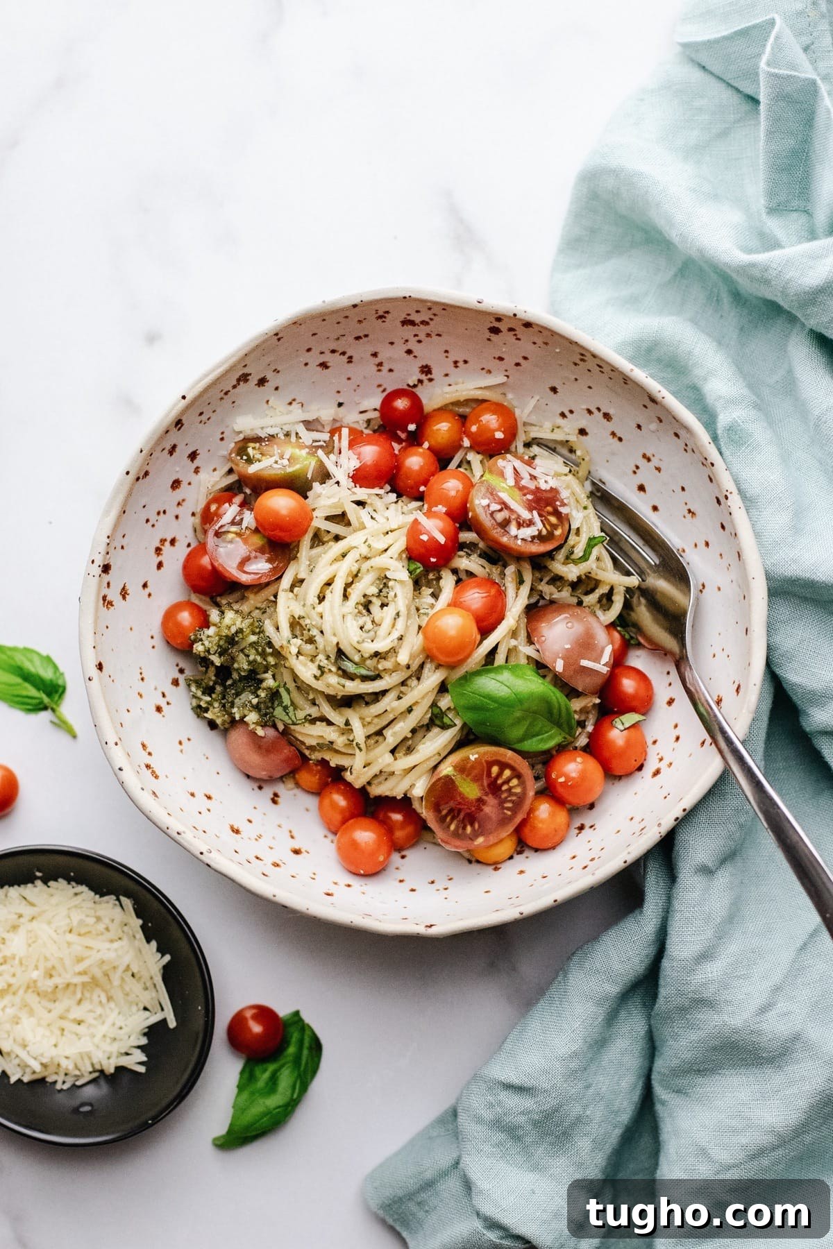 Pesto Spaghetti with Fresh Garden Tomatoes 6 A ceramic bowl with spaghetti and cherry tomatoes in it on a white counter with a blue napkin next to it.