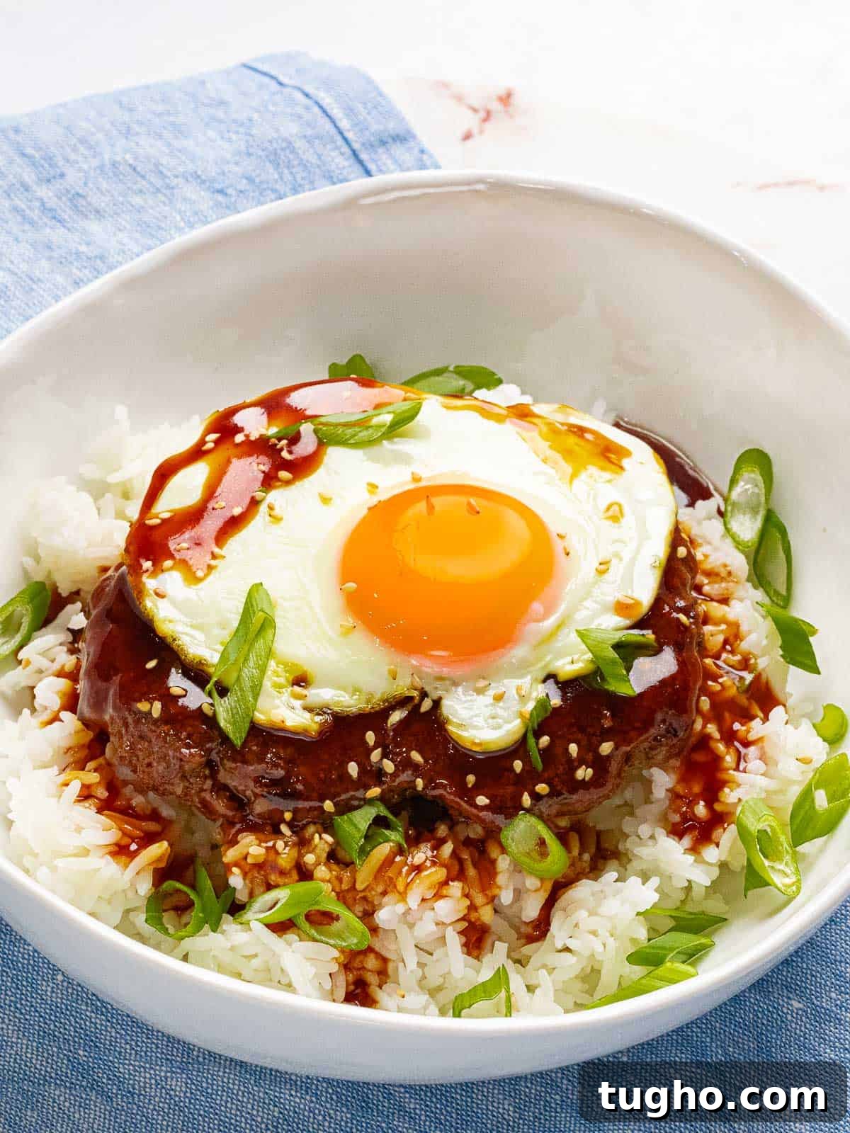 Loco Moco Recipe: Hawaiian Burger with Savory Brown Gravy 2 Hawaiian loco moco with a burger, gravy, white rice, and a sunny side up egg in a white bowl.