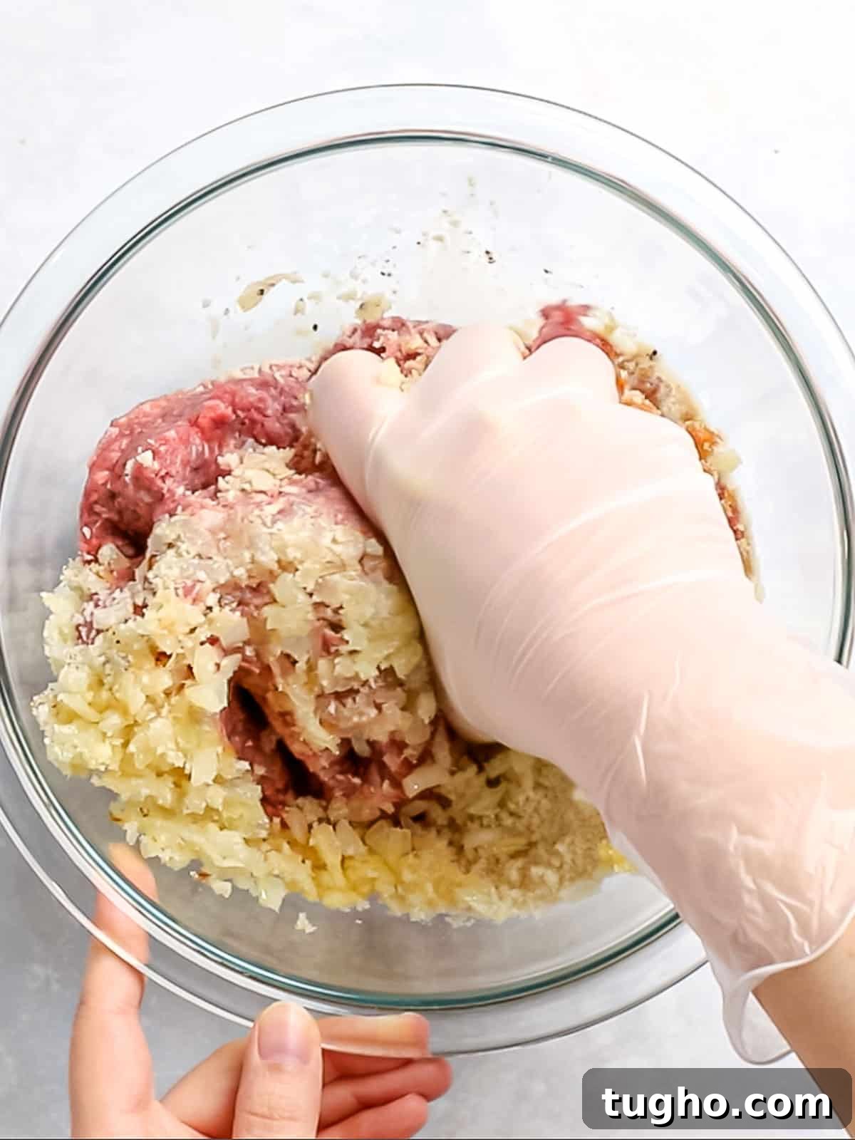 Loco Moco Recipe: Hawaiian Burger with Savory Brown Gravy 6 Loco moco patty being mixed with ground beef, onions, bread crumbs, and seasonings by a gloved hand.